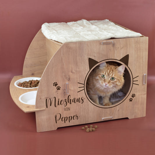 Katzenhaus in Eiche-Optik mit Aufdruck Miezhaus von Pepper, Katze in der runden Öffnung, oberem Kissen und Futterstation