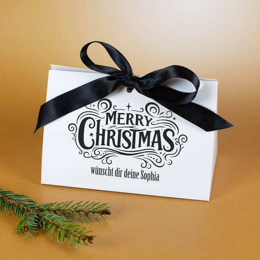Personalisierte Weihnachts-Geschenktasche mit schwarzer Schleife und Text „wünscht dir deine Sophia“ neben Tannenzweigen
