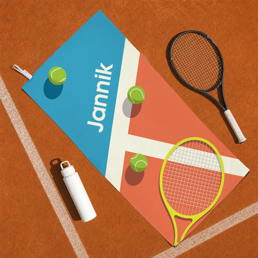 Personalisiertes Tennis Sporthandtuch mit Name Jannik auf Tennisplatz neben Tennisschläger und Trinkflasche