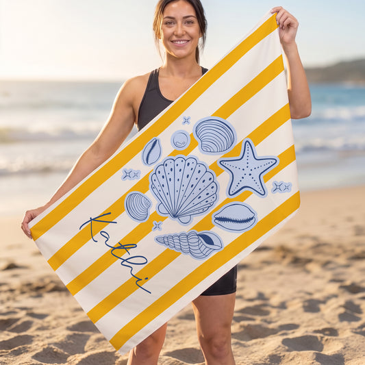 Person hält großes Strandhandtuch mit Muscheln, Seestern und personalisiertem Namen am Strand