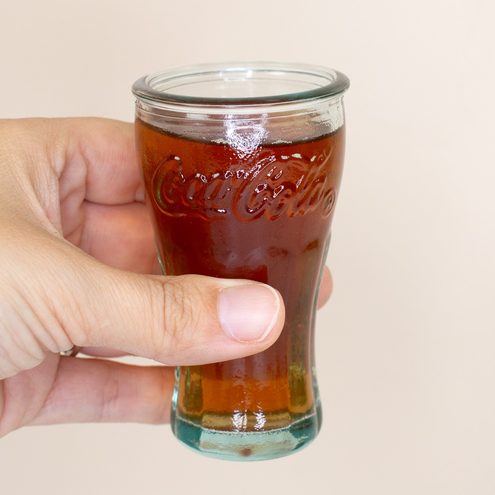 Coca-Cola Schnapsglas aus 100 % recyceltem Glas mit dunklem Getränk in der Hand