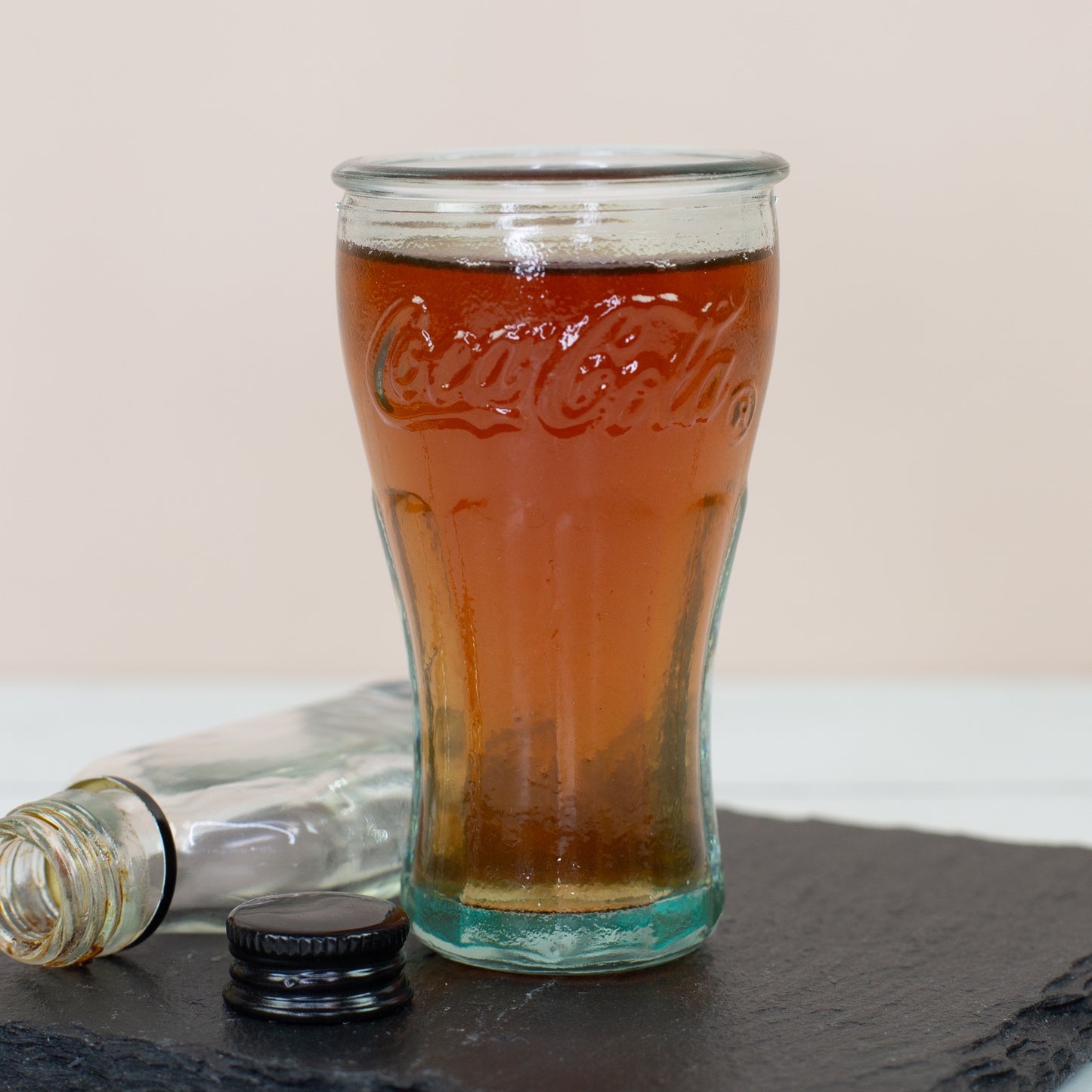 Gefülltes Coca-Cola Schnapsglas auf Schieferplatte mit kleiner Flasche im Hintergrund