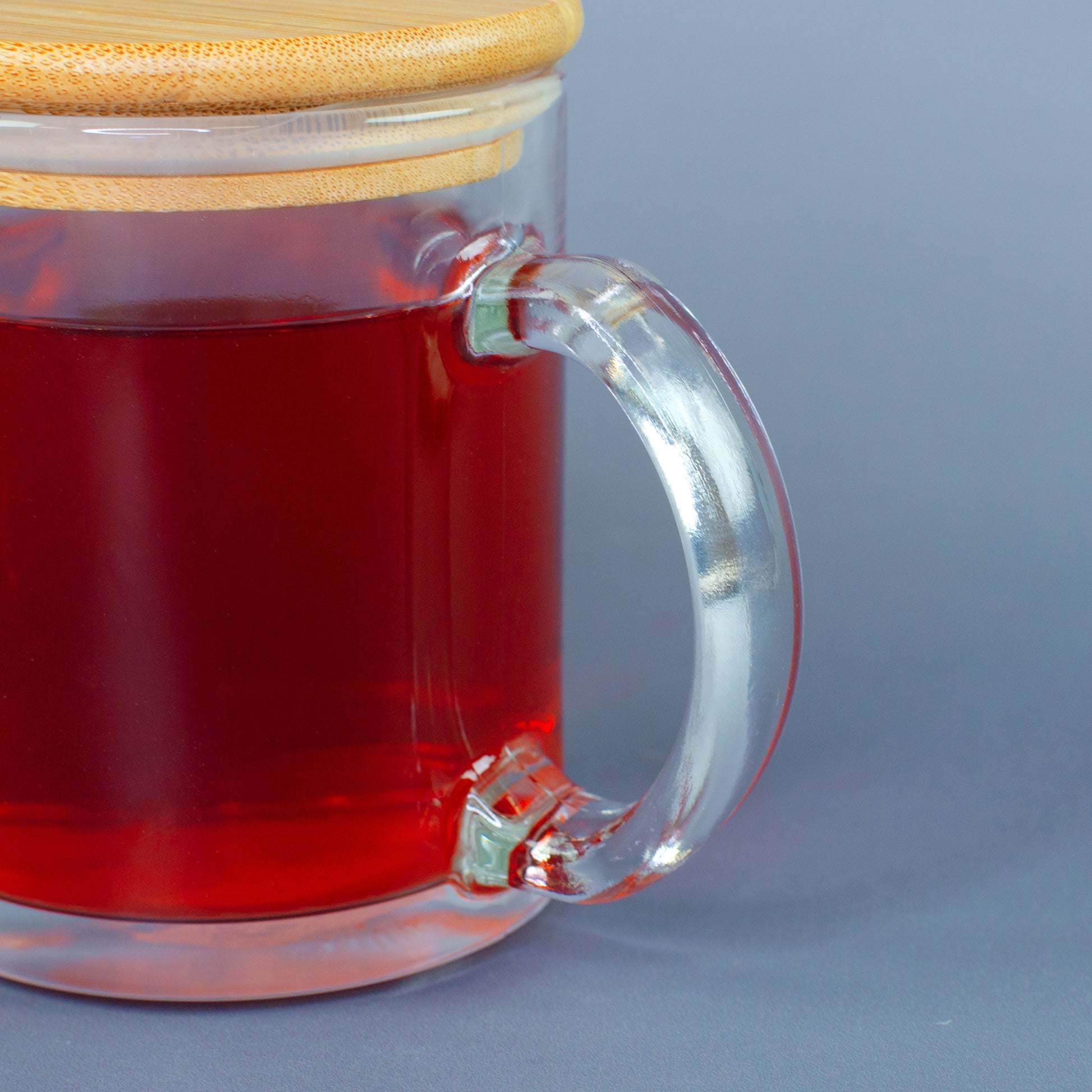 Nahaufnahme vom Glasgriff der Teeglastasse mit rotem Getränk und Bambusdeckel