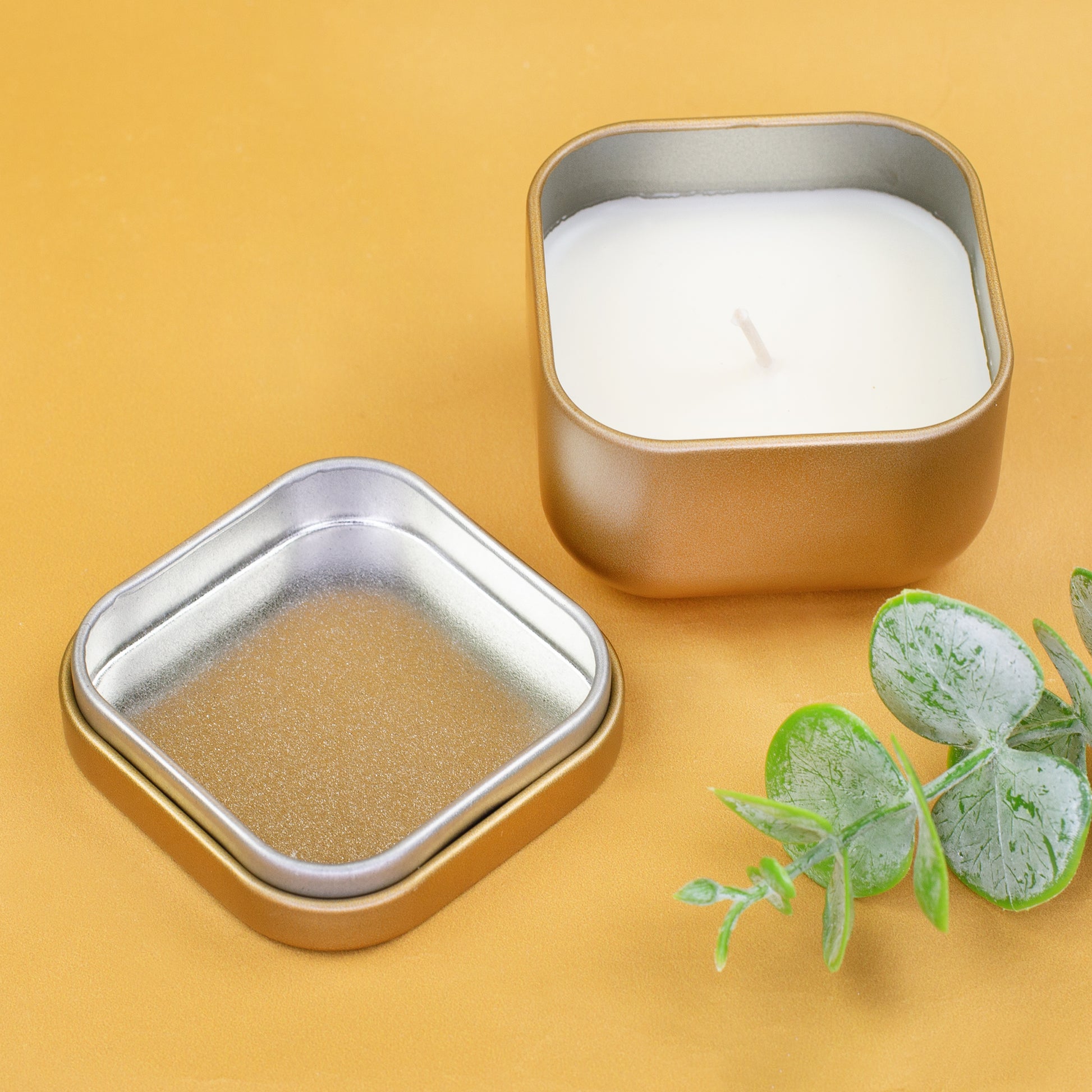 Geöffnete goldene Mini-Duftkerze mit Metalldeckel und weißem Wachs auf gelbem Hintergrund