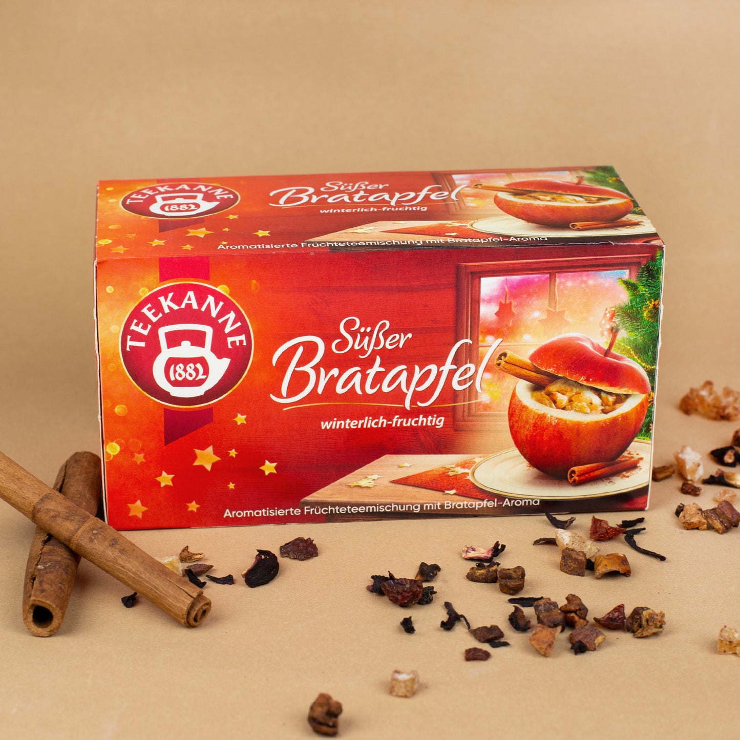 Packung Teekanne Wintertee "Süßer Bratapfel" dekoriert mit Zimtstangen und losem Tee auf braunem Hintergrund