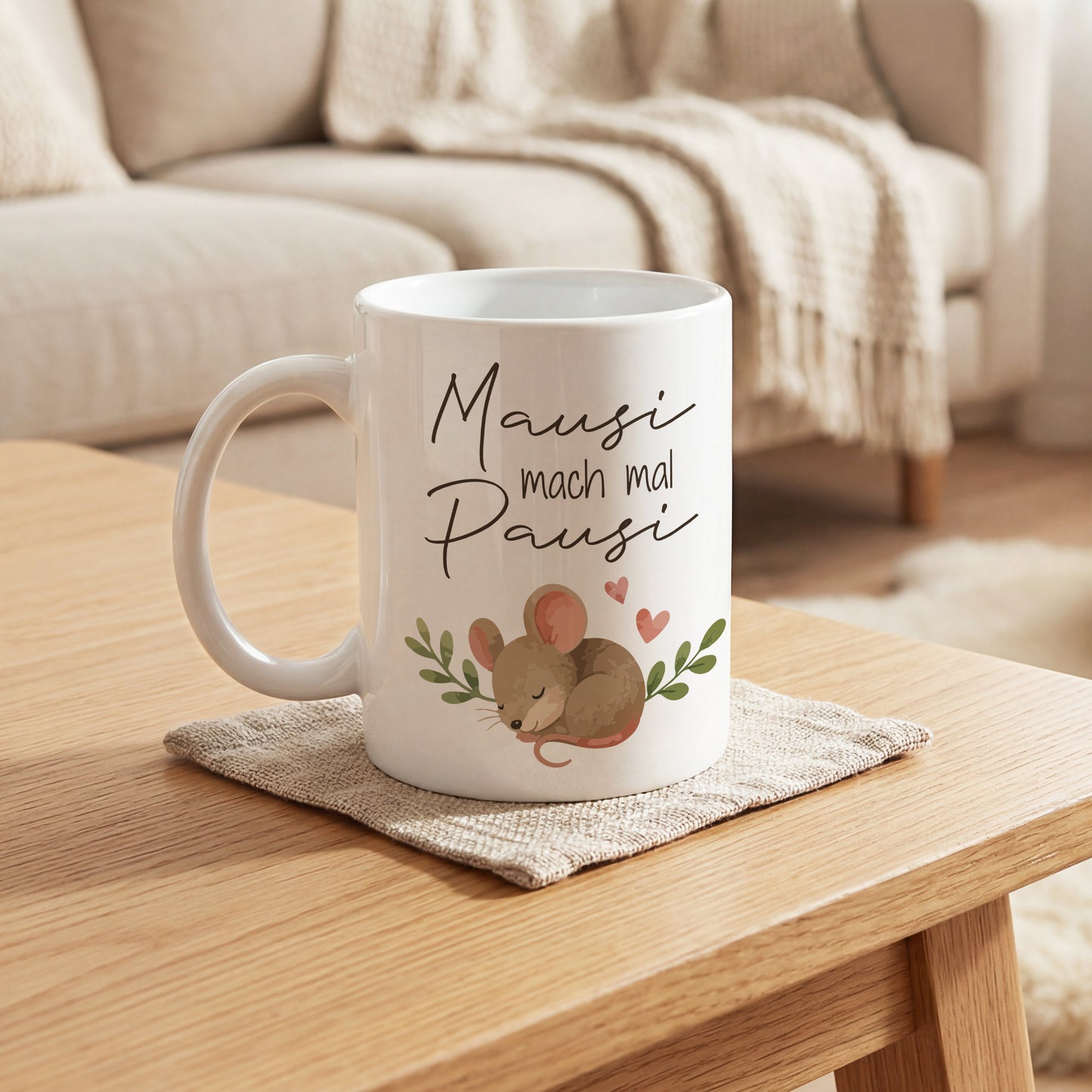 Weiße Kaffeetasse mit Mausi mach mal Pausi Motiv auf Tisch vor Sofa