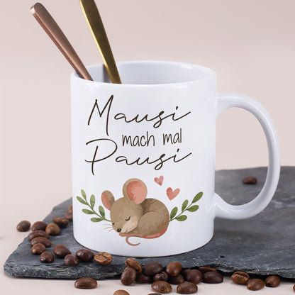 Weiße Keramiktasse mit Mausi mach mal Pausi Motiv und Löffeln auf Schieferplatte