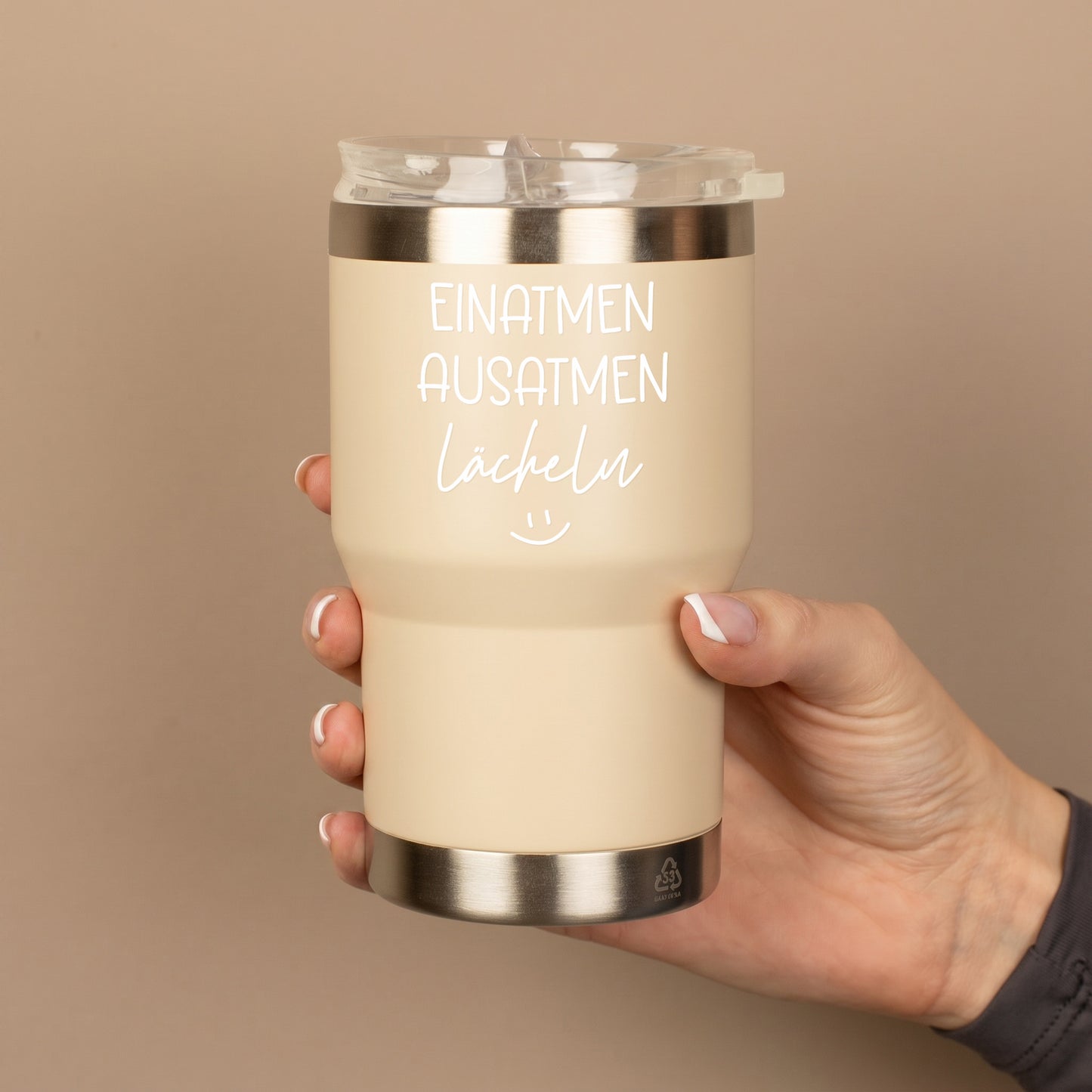 Beiger Thermobecher mit Spruch Einatmen Ausatmen Lächeln wird in der Hand gehalten