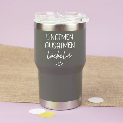Grauer Thermobecher mit Deckel und Spruch Einatmen Ausatmen Lächeln auf hellem Hintergrund