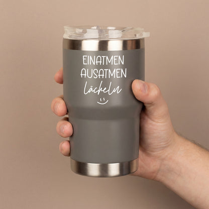 Grauer Thermobecher mit Spruch Einatmen Ausatmen Lächeln in der Hand