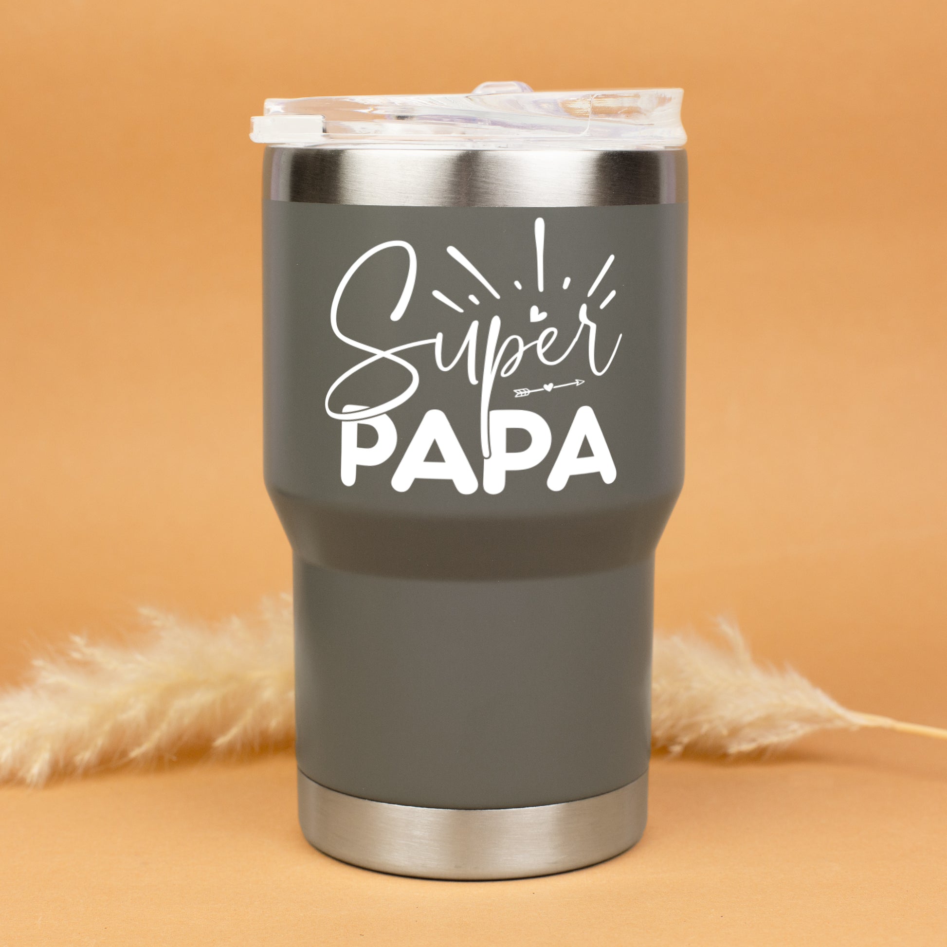Grauer Thermobecher mit Super Papa Aufdruck freigestellt vor warmem Hintergrund