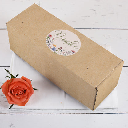 Längliche Geschenkbox mit floraler Danke-Aufschrift im Kraftpapier-Look – dekorativ auf weißem Tuch mit orangefarbener Rose