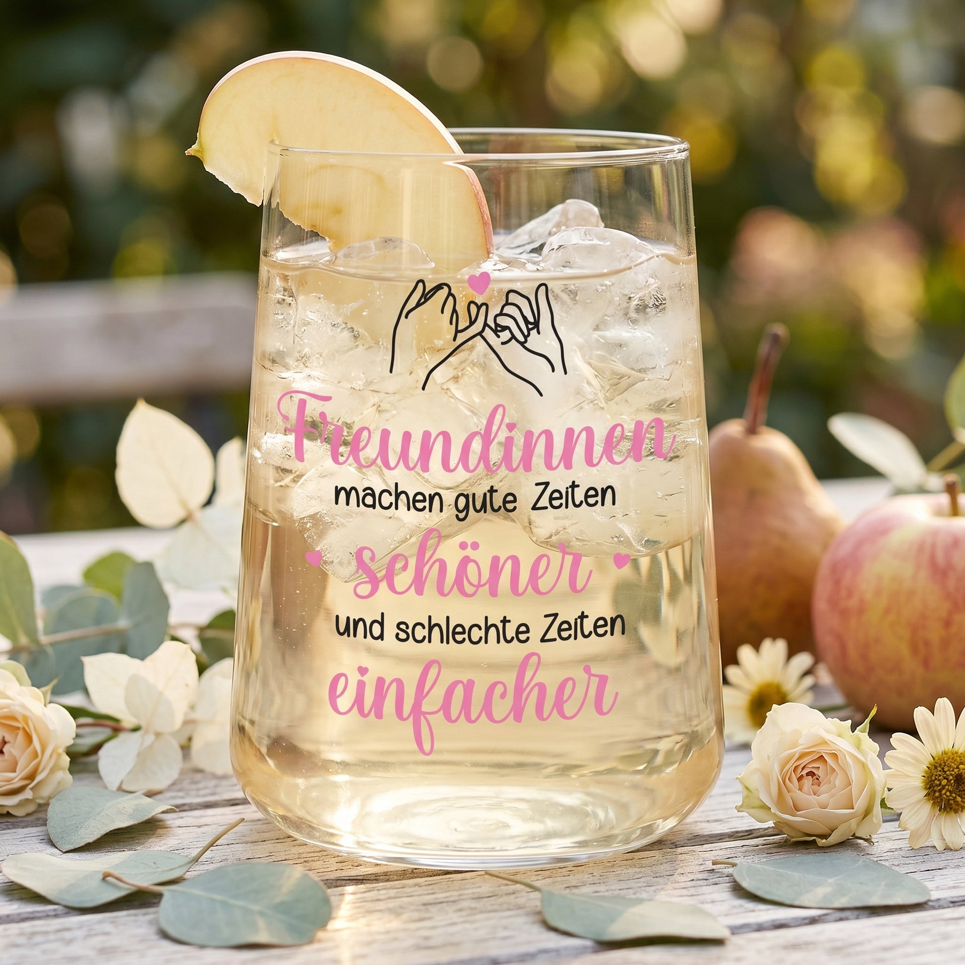 Trinkglas mit hellem Getränk, Eiswürfeln, Apfelscheibe und Freundinnen-Spruch im Gartenambiente