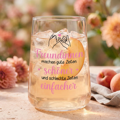 Trinkglas mit hellem Getränk, Eiswürfeln, Pfirsichscheibe und Spruch für Freundinnen im floralen Ambiente