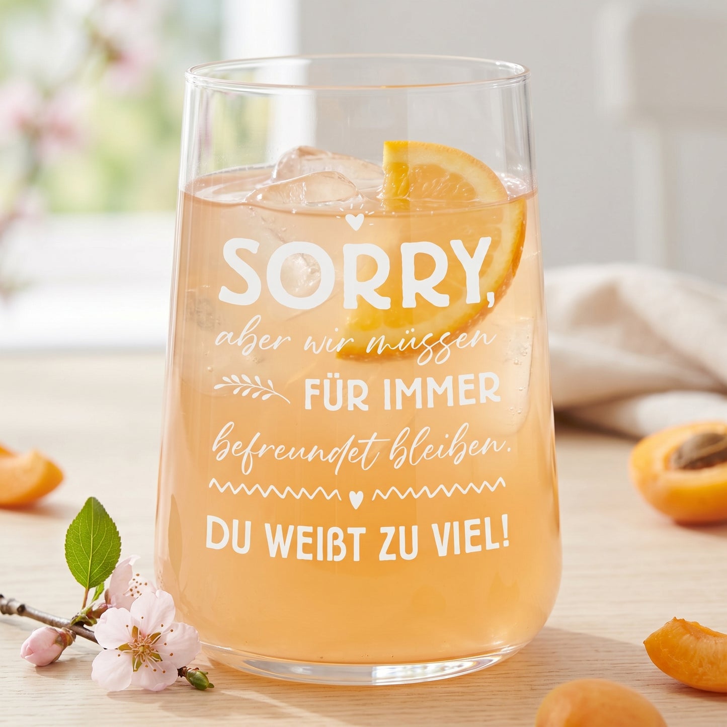 Trinkglas mit hellem Fruchtgetränk, Eiswürfeln, Orange und Spruch für Freundinnen