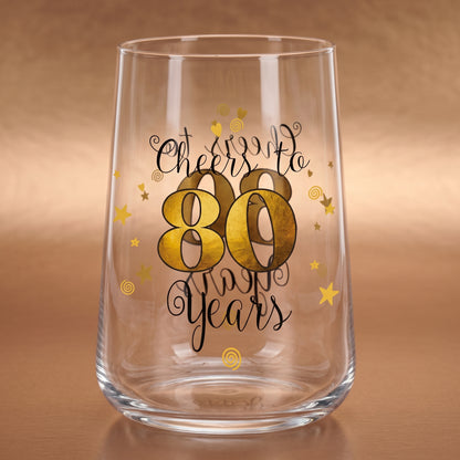 Leeres Trinkglas zum 80. Geburtstag mit goldener 80 und dekorativen Sternen auf warmem Holzuntergrund