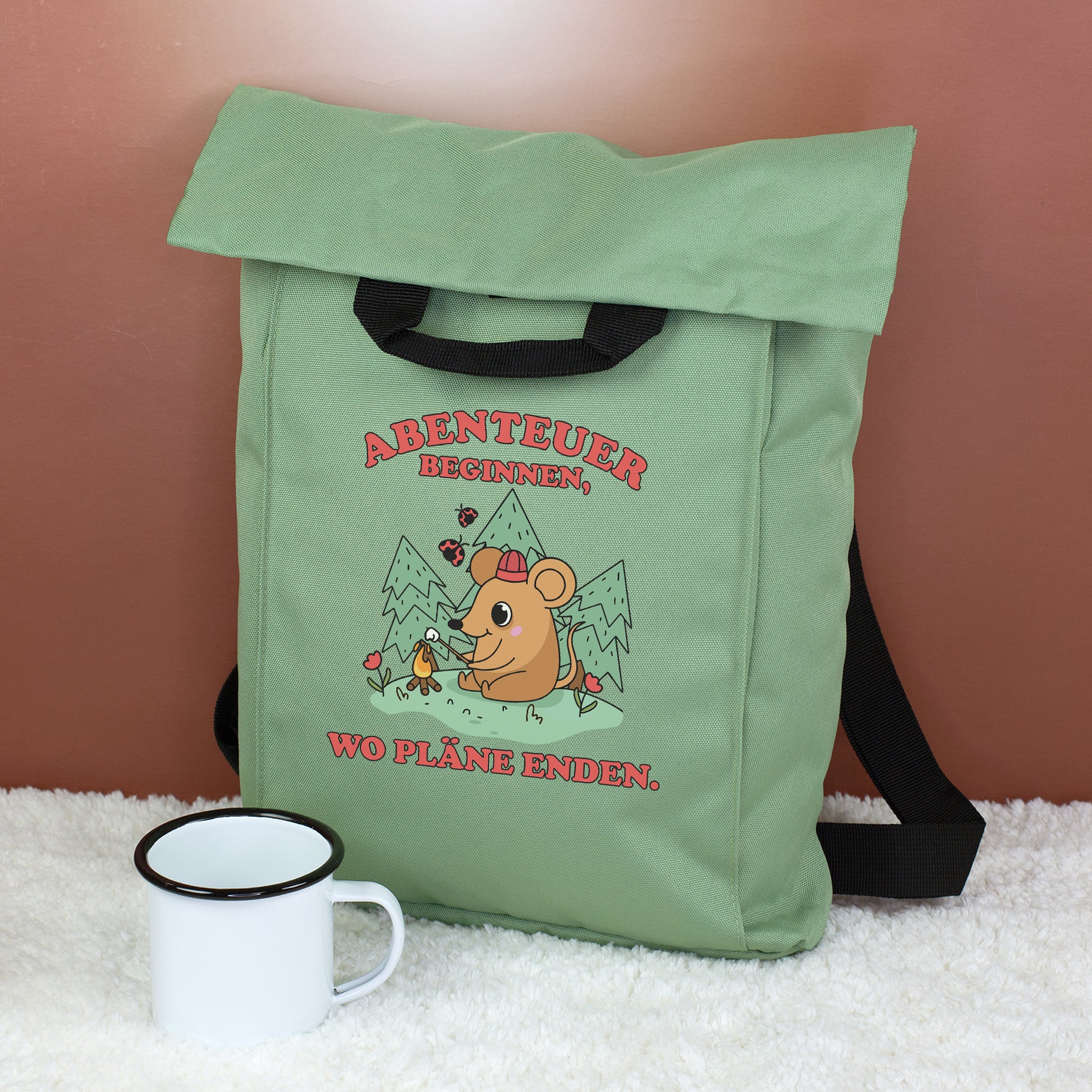 Jadegrüner Rucksack mit Abenteuer-Maus Motiv, Campingmaus, Bergen und Spruch auf flauschigem Untergrund