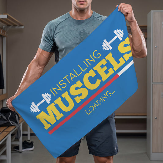 Person hält blaues Sporthandtuch mit lustigem Installing Muscles Loading Aufdruck im Fitnessstudio