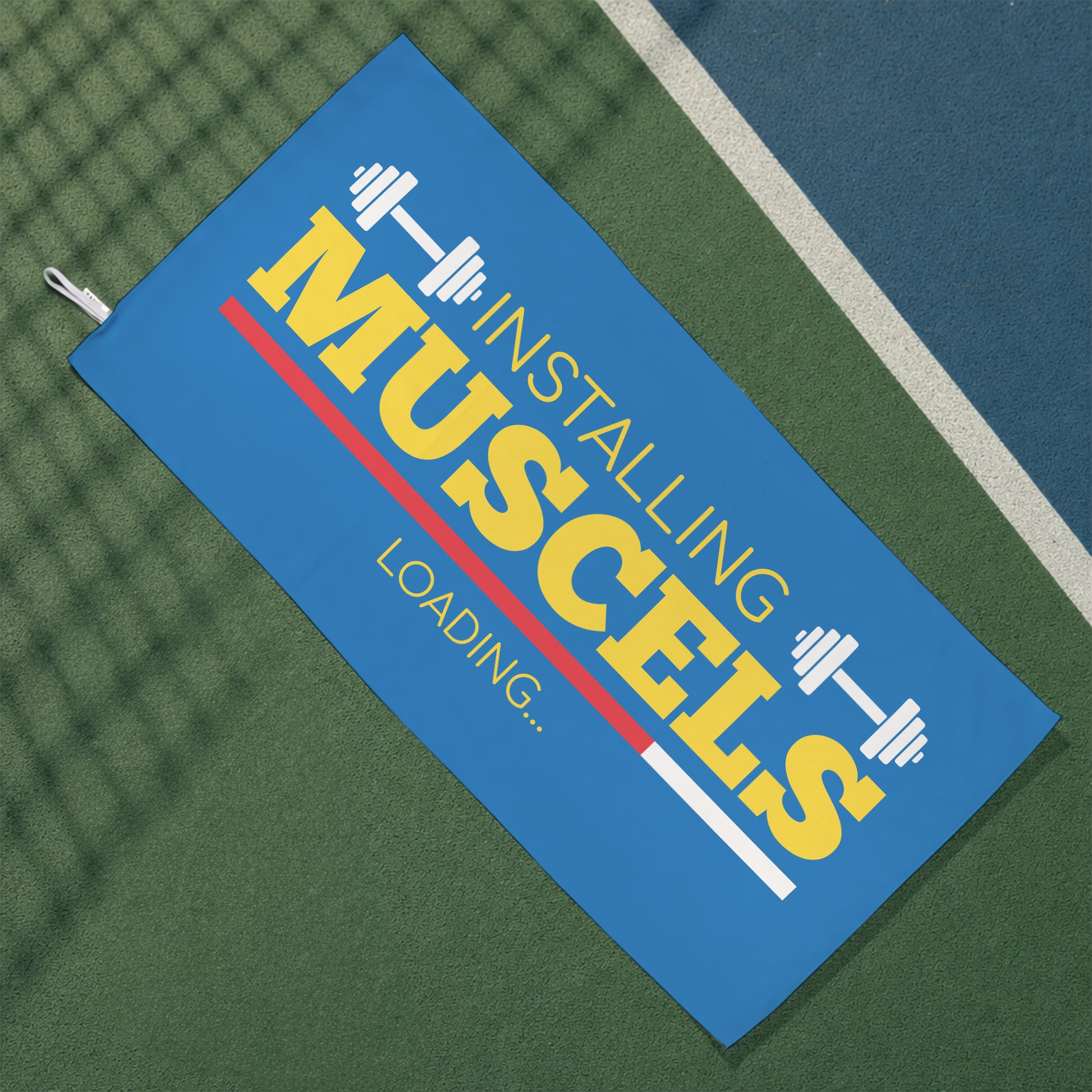 Blaues Gym Handtuch mit Hantelmotiv und Installing Muscles Loading Schriftzug auf Sportplatz