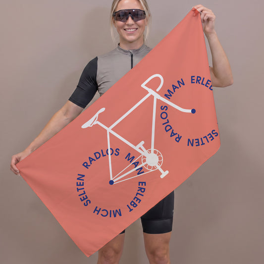 Frau hält korallfarbenes Sporthandtuch mit weißem Rennrad-Aufdruck und blauem Schriftzug Radlos man erlebt mich selten
