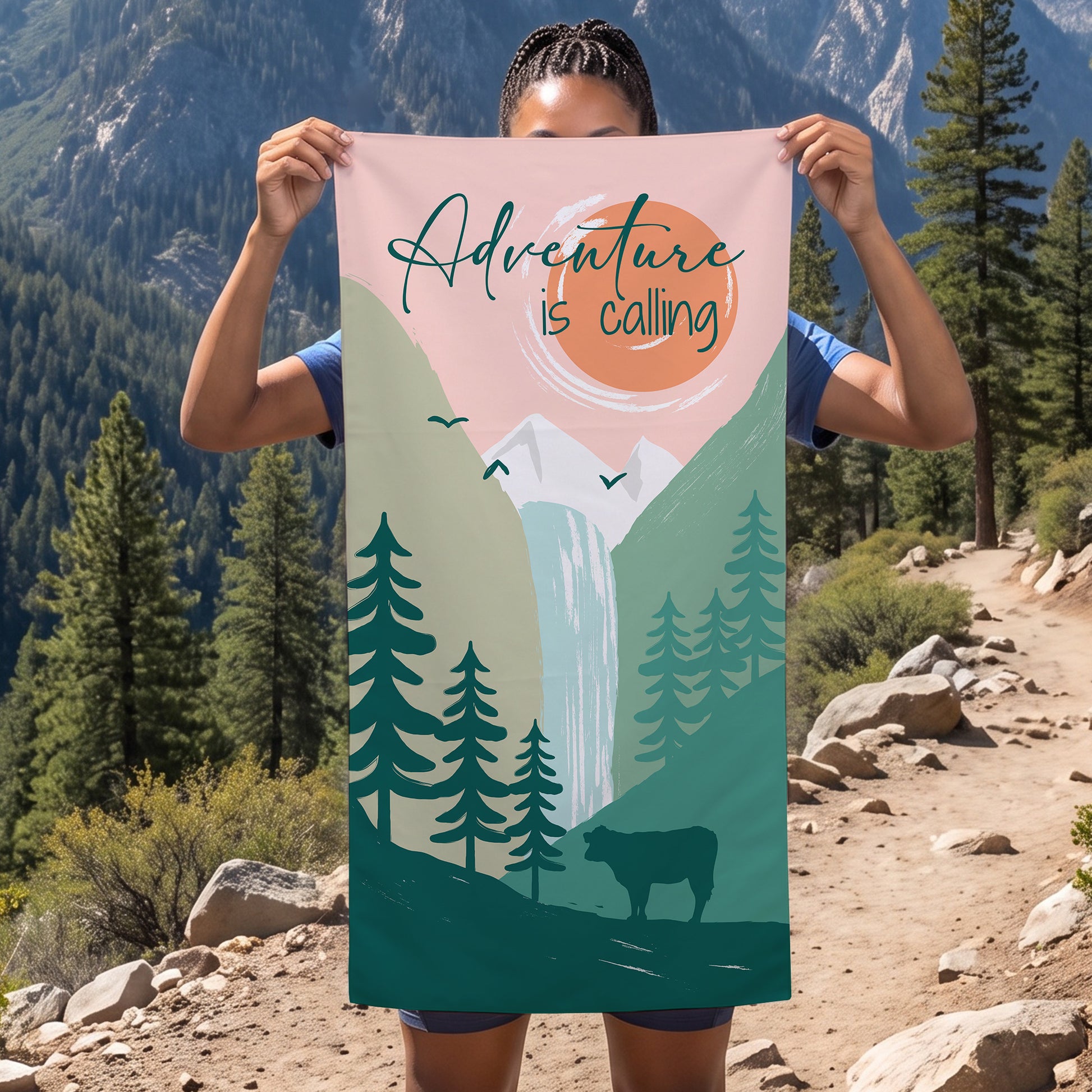 Person hält Sporthandtuch mit Abenteuer-Motiv vor Berglandschaft, Aufdruck mit Bergen, Wasserfall und Schriftzug Adventure is calling