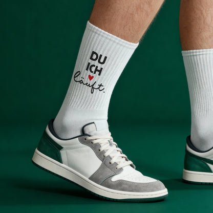 Detailansicht der weißen Socken am Bein vor grünem Hintergrund, Motiv „DU ICH läuft.“ mit Herz