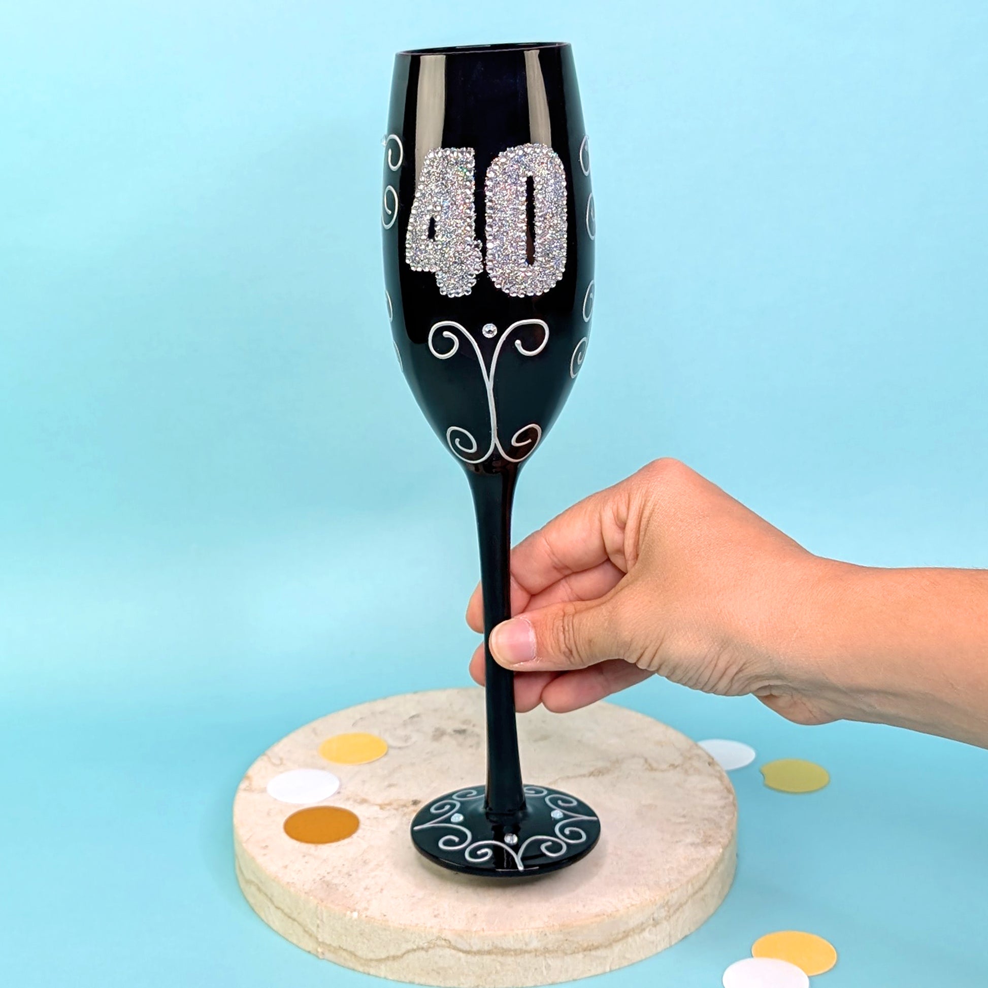 Schwarzes Sektglas mit glitzernder 40 und Ornamenten, frontal fotografiert, gehalten von einer Hand