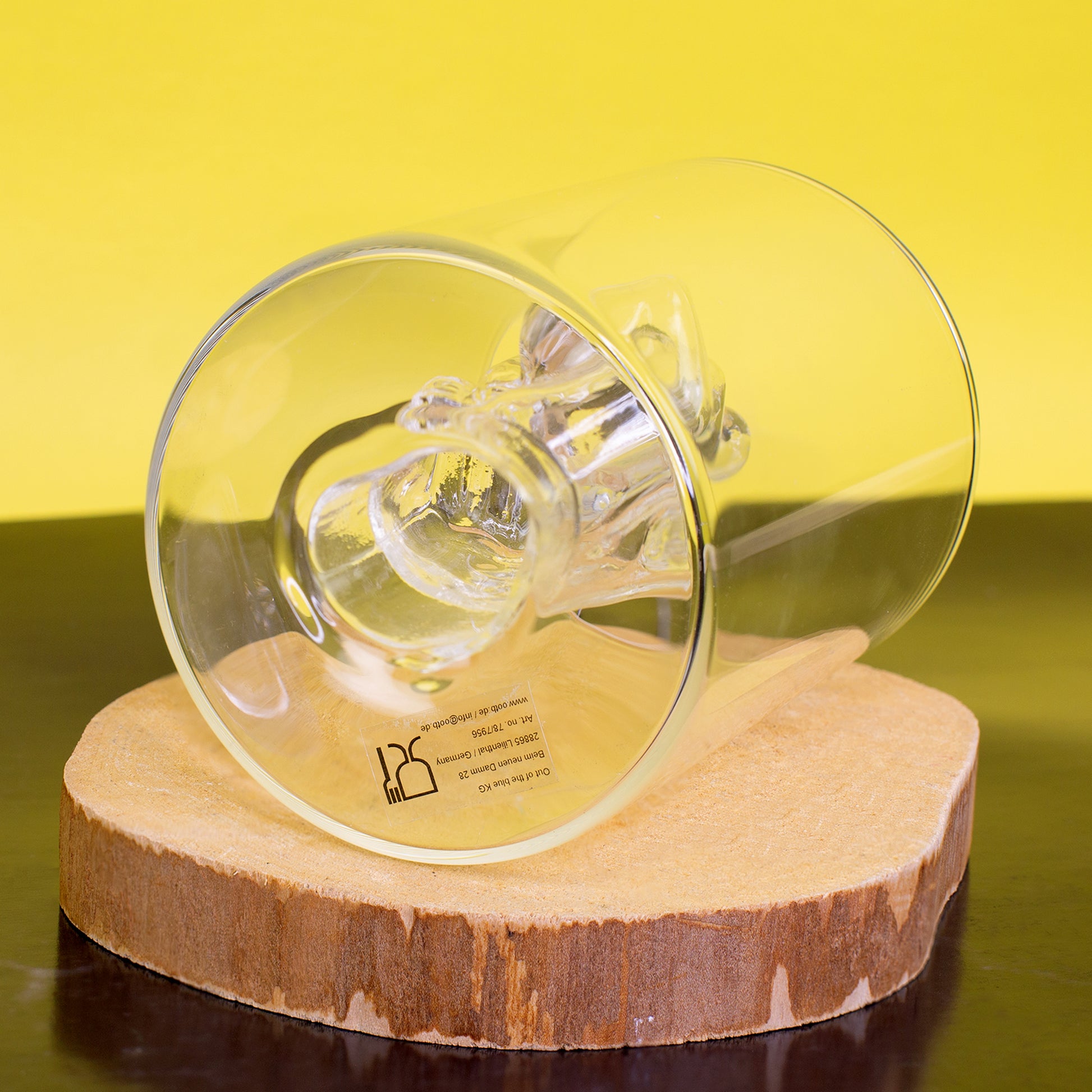Trinkglas mit Mittelfinger Figur liegend auf Holzscheibe vor gelbem Hintergrund
