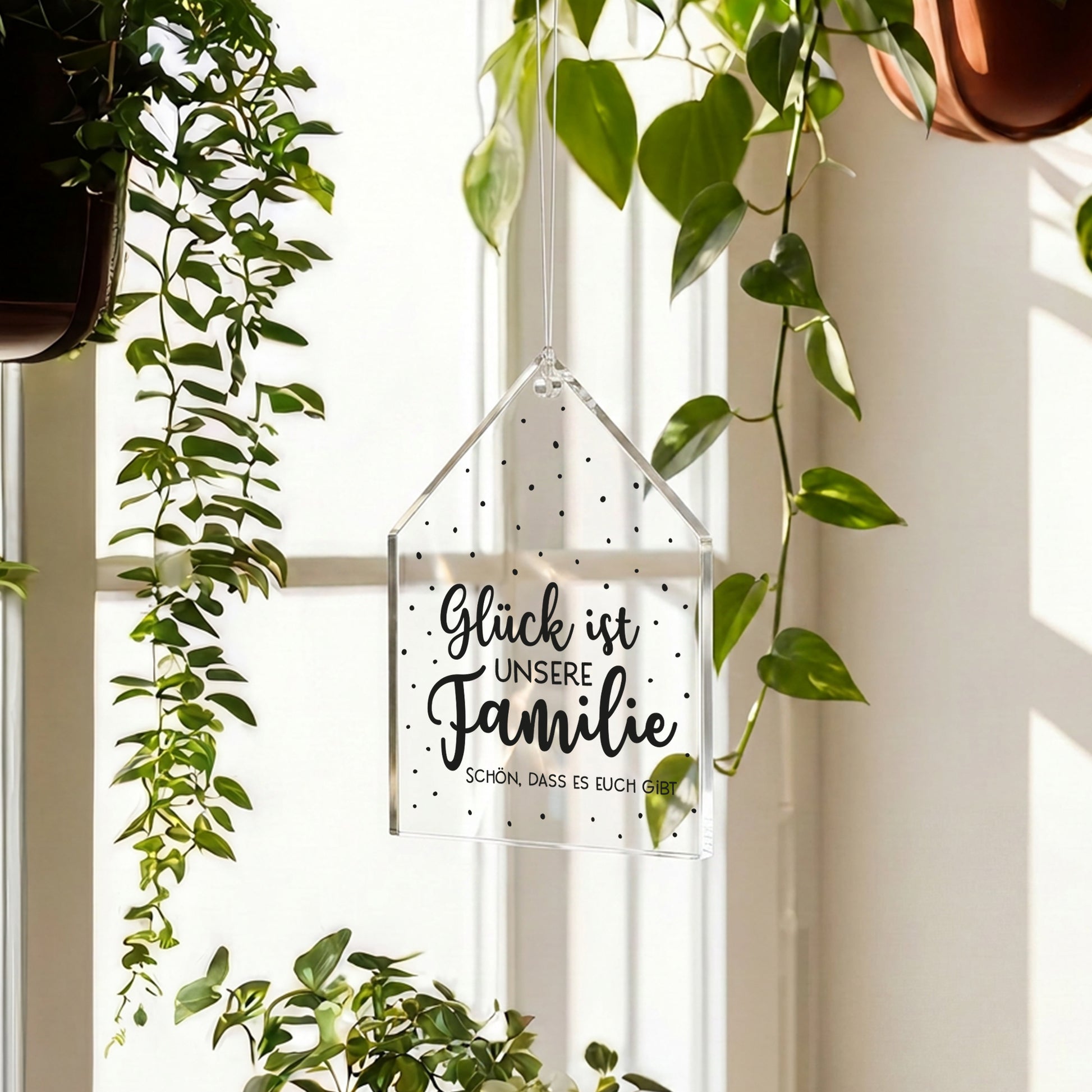 Transparenter Acrylanhänger Glück ist unsere Familie hängt am Fenster zwischen grünen Pflanzen