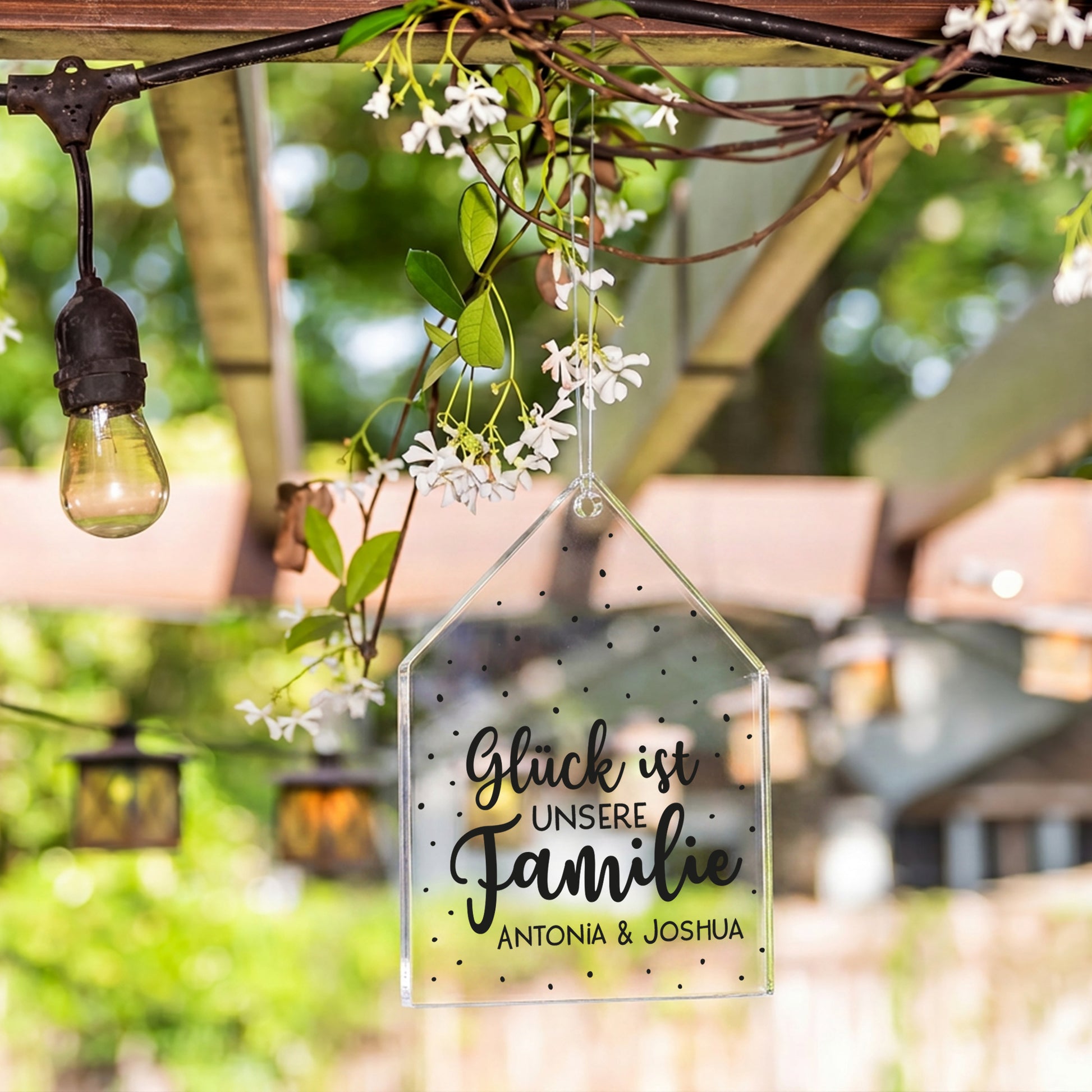 Personalisierter Acrylanhänger in Hausform mit Namen Antonia und Joshua hängt als Gartendeko im Außenbereich