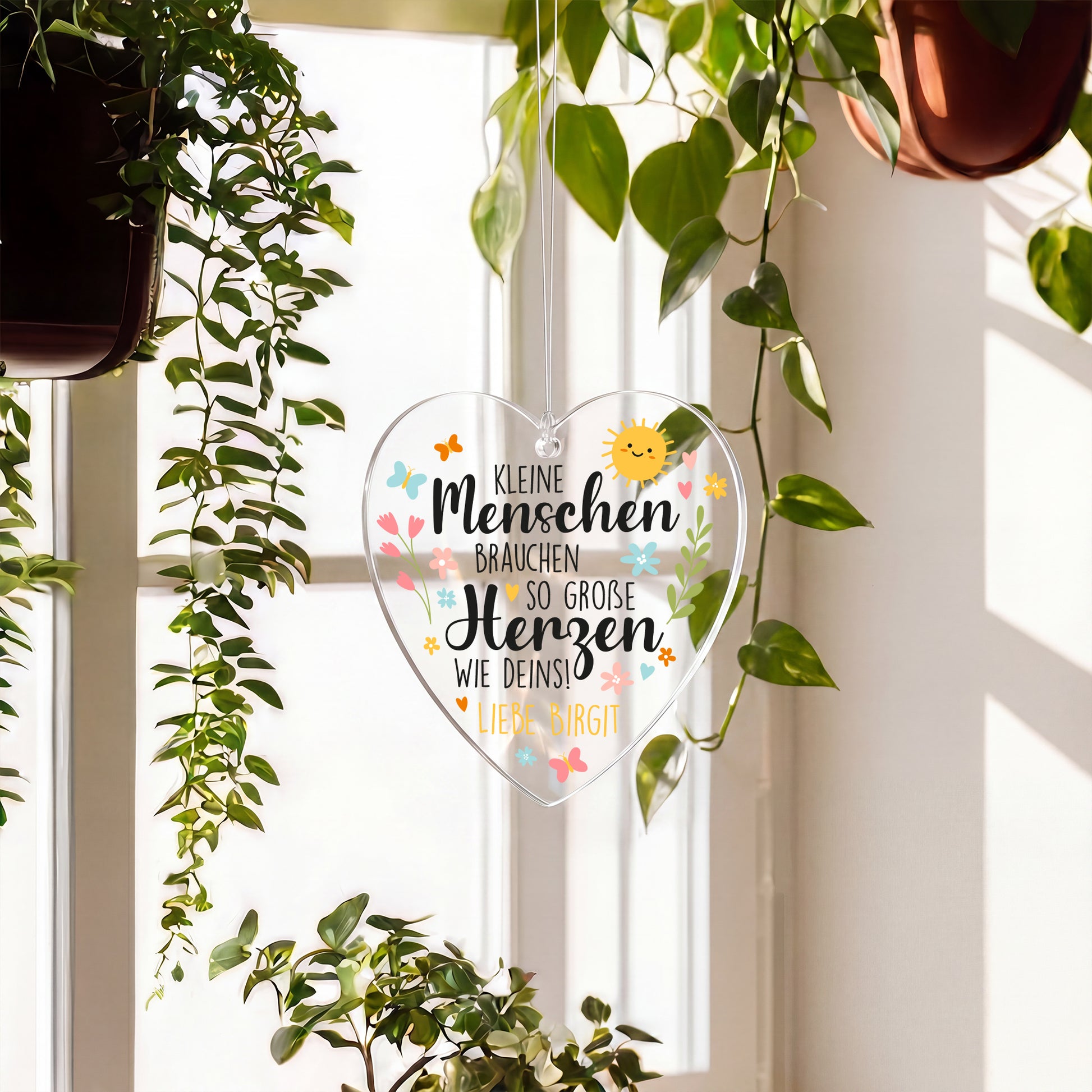 Transparentes Deko-Herz aus Acryl mit liebevollem Spruch und Text Liebe Birgit am Fenster zwischen Pflanzen
