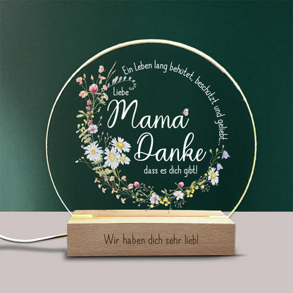 LED-Nachtlicht mit personalisierbarer Gravur auf dem Holzsockel, gestaltet als liebevolles Geschenk für Mama. Die Acrylplatte zeigt einen Kranz aus Frühlingsblumen mit dem Spruch „Ein Leben lang behütet, beschützt und geliebt... Liebe Mama, Danke, dass es dich gibt!“. Warmweißes LED-Licht sorgt für eine stimmungsvolle Beleuchtung – ideal als Muttertagsgeschenk oder liebevolle Überraschung.