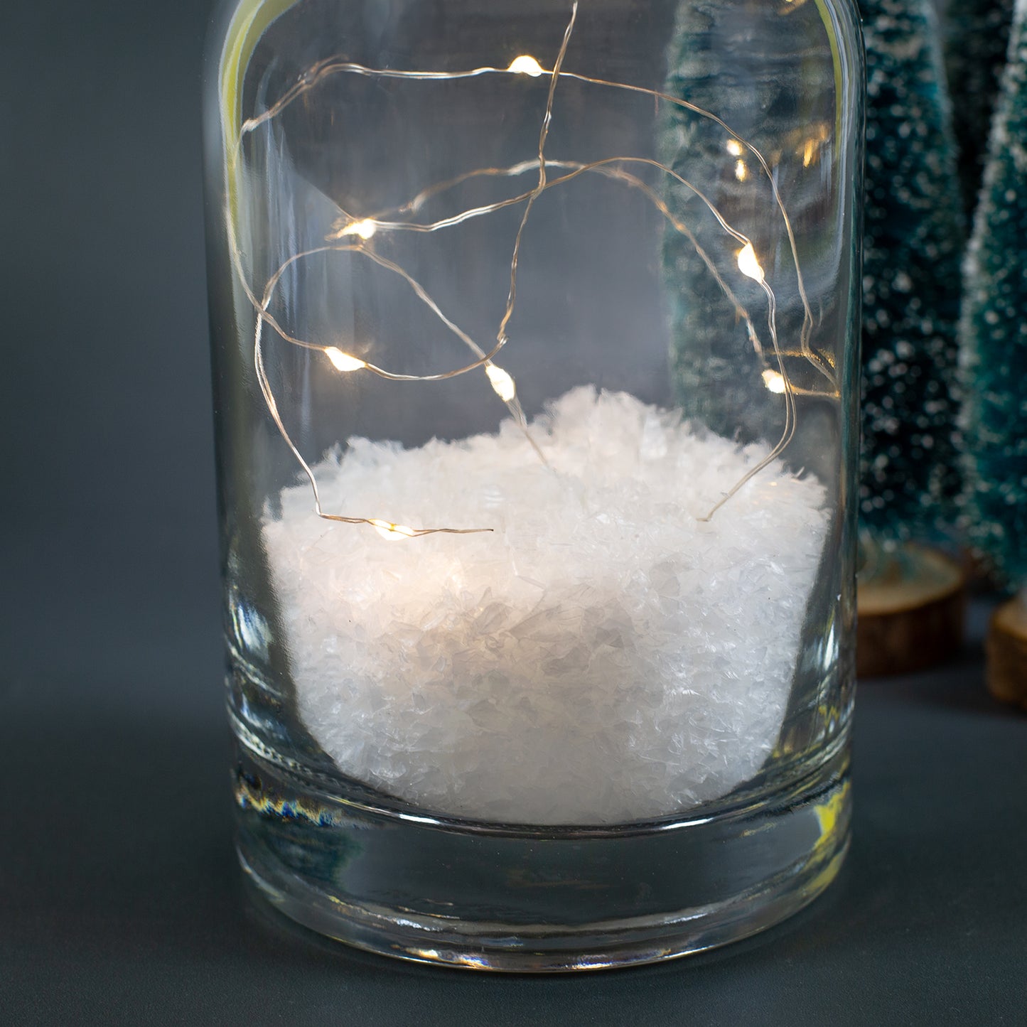 Detailaufnahme der Deko-Karaffe mit Kunstschnee und LED-Lichterkette im Inneren, warmweiße Lichtpunkte vor dunklem Hintergrund.
