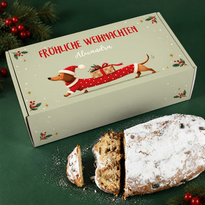 Personalisierte Stollen Geschenkbox mit Dackel in Weihnachtskleidung neben angeschnittenem Rosinenstollen