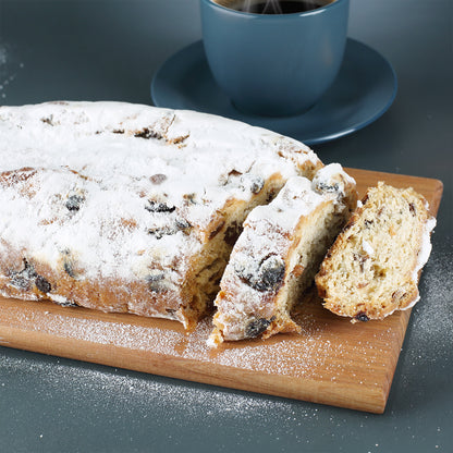 Nahaufnahme vom angeschnittenen Rosinenstollen mit Puderzucker, Sultaninen und Mandeln neben einer Tasse Kaffee