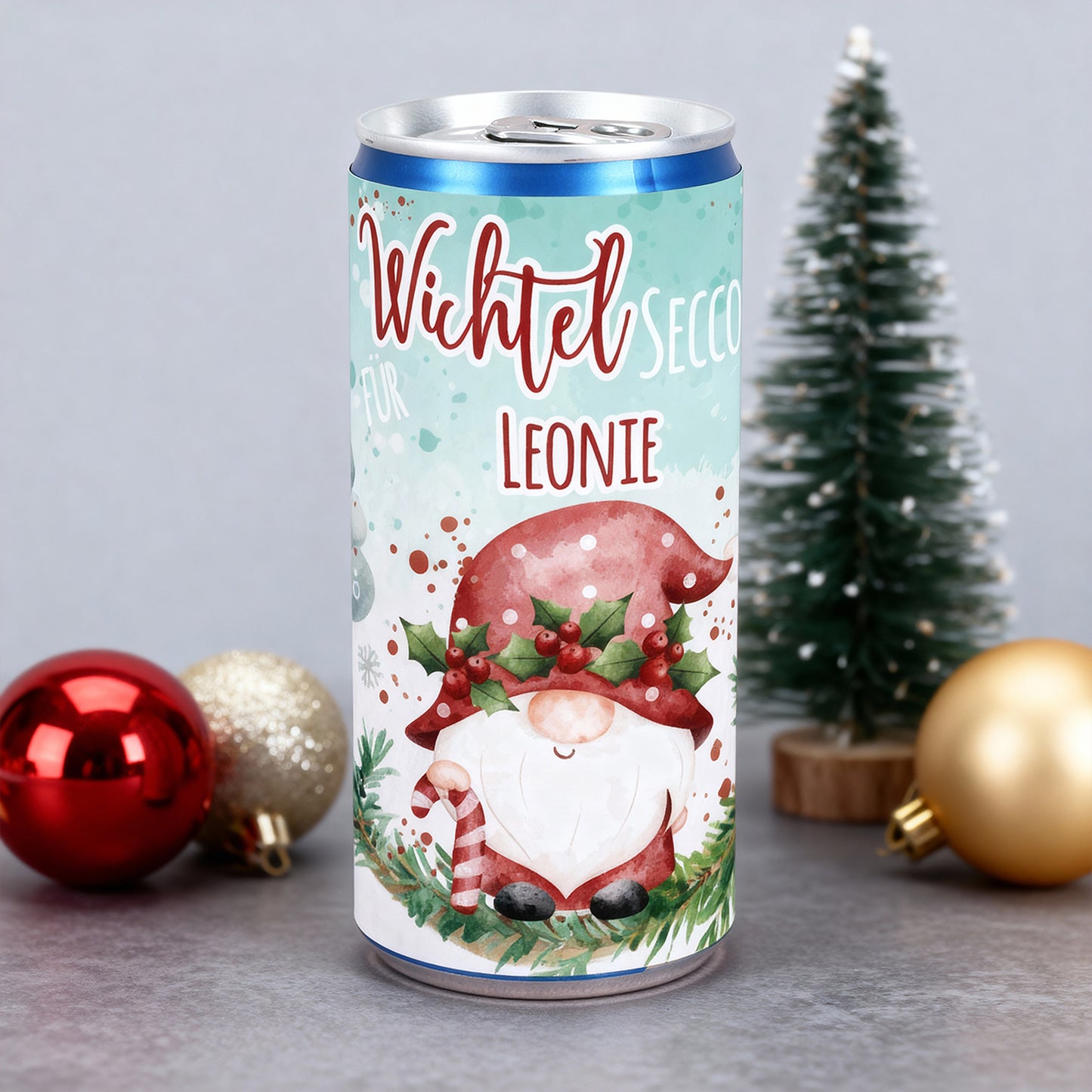 Secco-Dose Wichtel Secco mit Name Leonie, stehend vor kleiner Weihnachtsbaum-Deko und roten Kugeln.