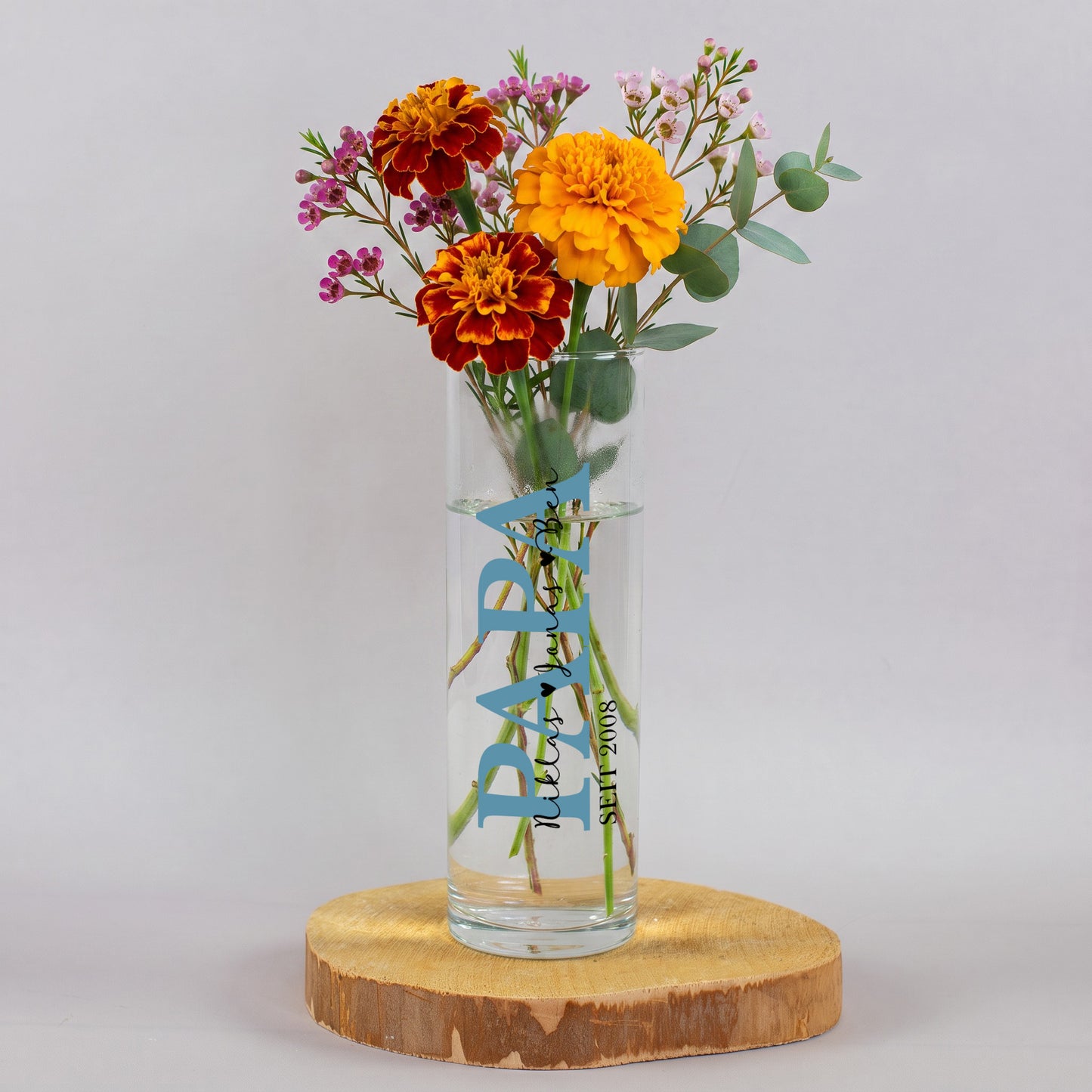 Schmale Blumenvase aus Glas mit blauem Papa Motiv, mehreren Kindernamen und Jahreszahl 2008, gefüllt mit bunten Blumen als Geschenk für Papa