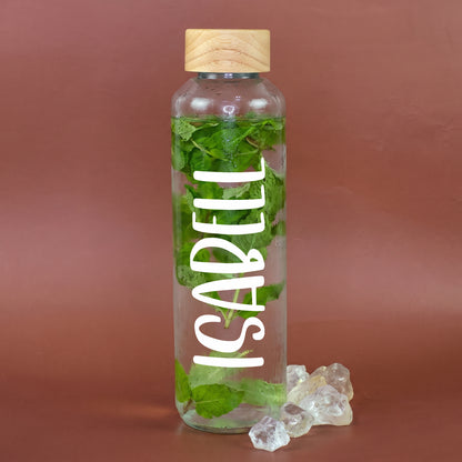 Personalisierte Trinkflasche aus recyceltem Glas mit weißem Namensaufdruck Isabell, gefüllt mit Wasser und frischer Minze, mit Holzdeckel