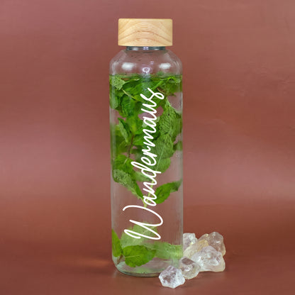 Glas Trinkflasche mit Holzdeckel und weißem Schriftzug Wandermaus, gefüllt mit Wasser und frischer Minze