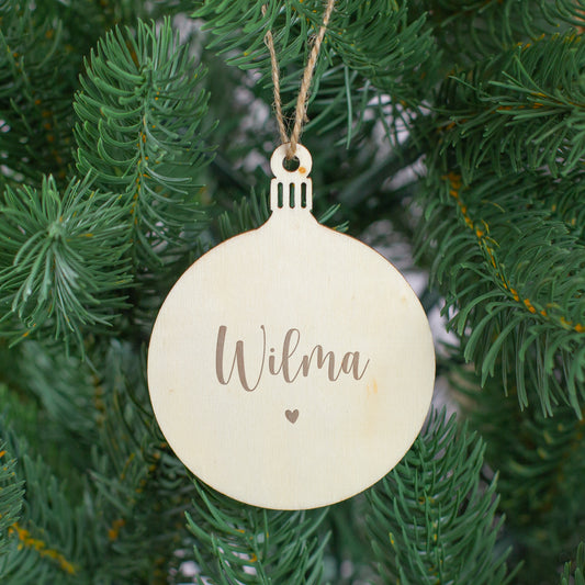 Weihnachtsanhänger aus Holz in Kugelform mit Gravur „Wilma“ und kleinem Herz, aufgehängt im Tannenbaum.