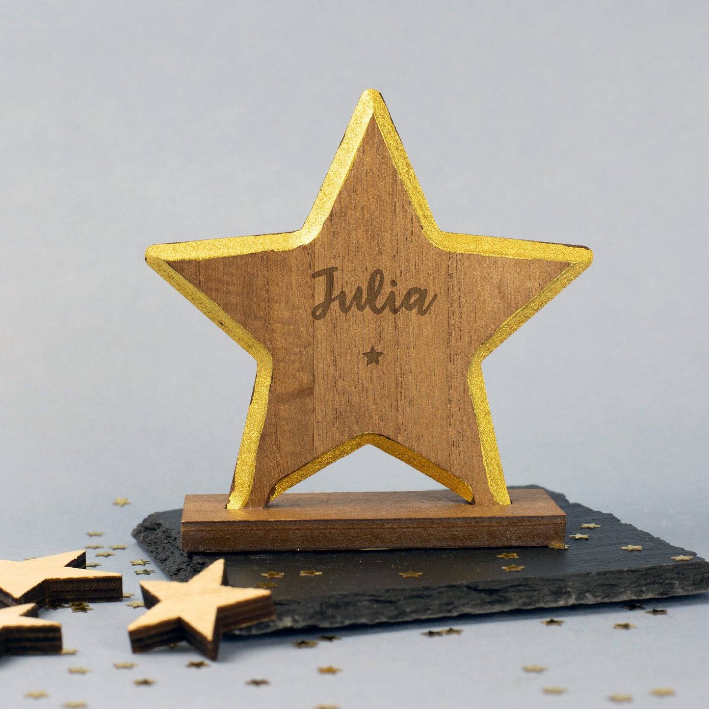 Holzstern mit goldenem Rand und graviertem Namen auf dem Sockel, darunter ein kleiner eingravierter Stern – festliche Weihnachtsfigur auf hellem Untergrund.