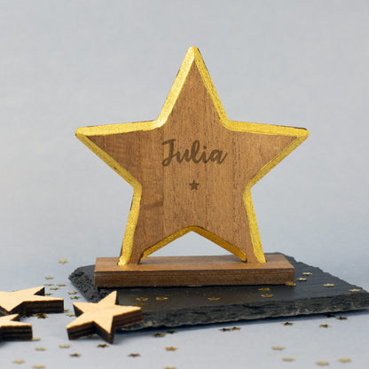 Holzstern mit goldenem Rand und graviertem Namen auf dem Sockel, darunter ein kleiner eingravierter Stern – festliche Weihnachtsfigur auf hellem Untergrund.