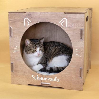 Getigerte Katze liegt in Katzenhaus in Holzoptik mit Katzenohren Motiv und Name Schnurrsula