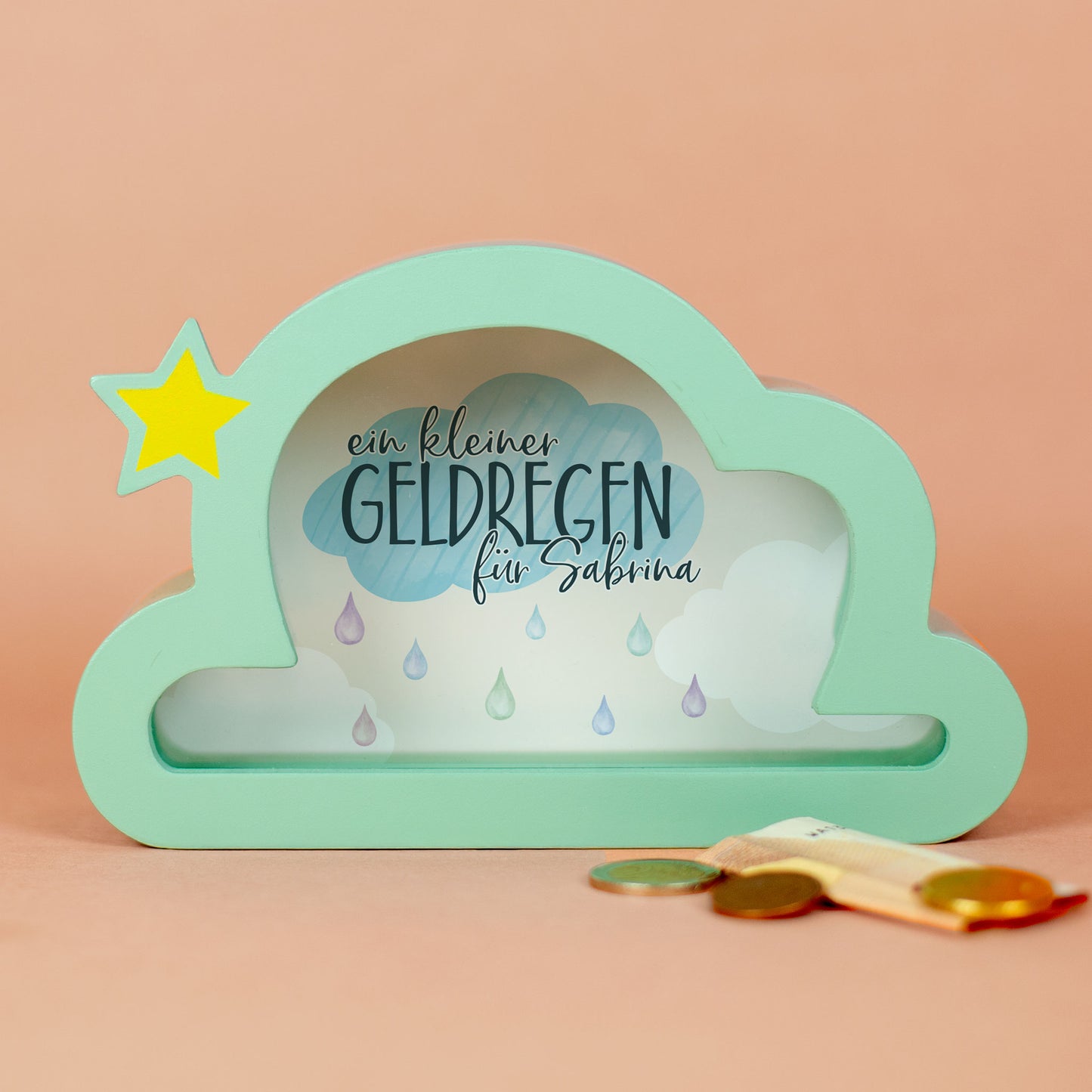 Spardose in Wolkenform mit gelbem Stern und Spruch "ein kleiner Geldregen für Sabrina" auf rosa Hintergrund.