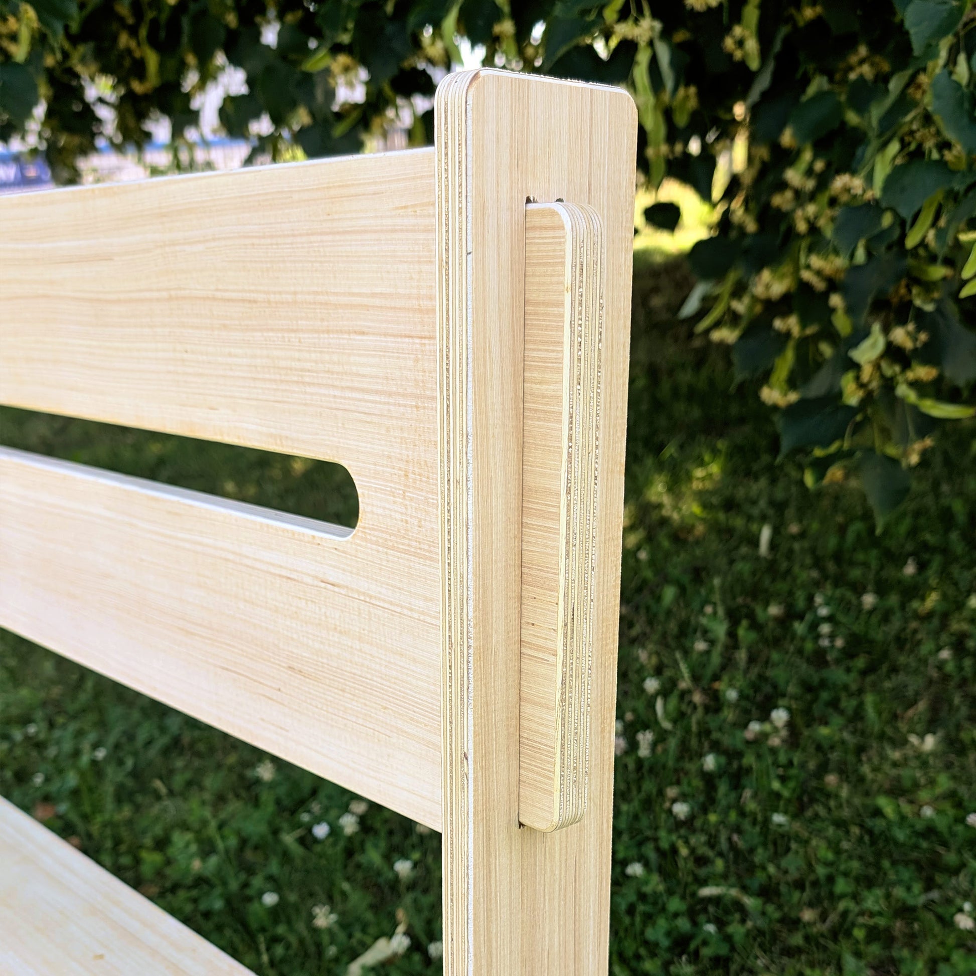 Detailansicht der seitlichen Verzapfung der Rückenlehne der gravierten Holzbank, vor grünem Hintergrund