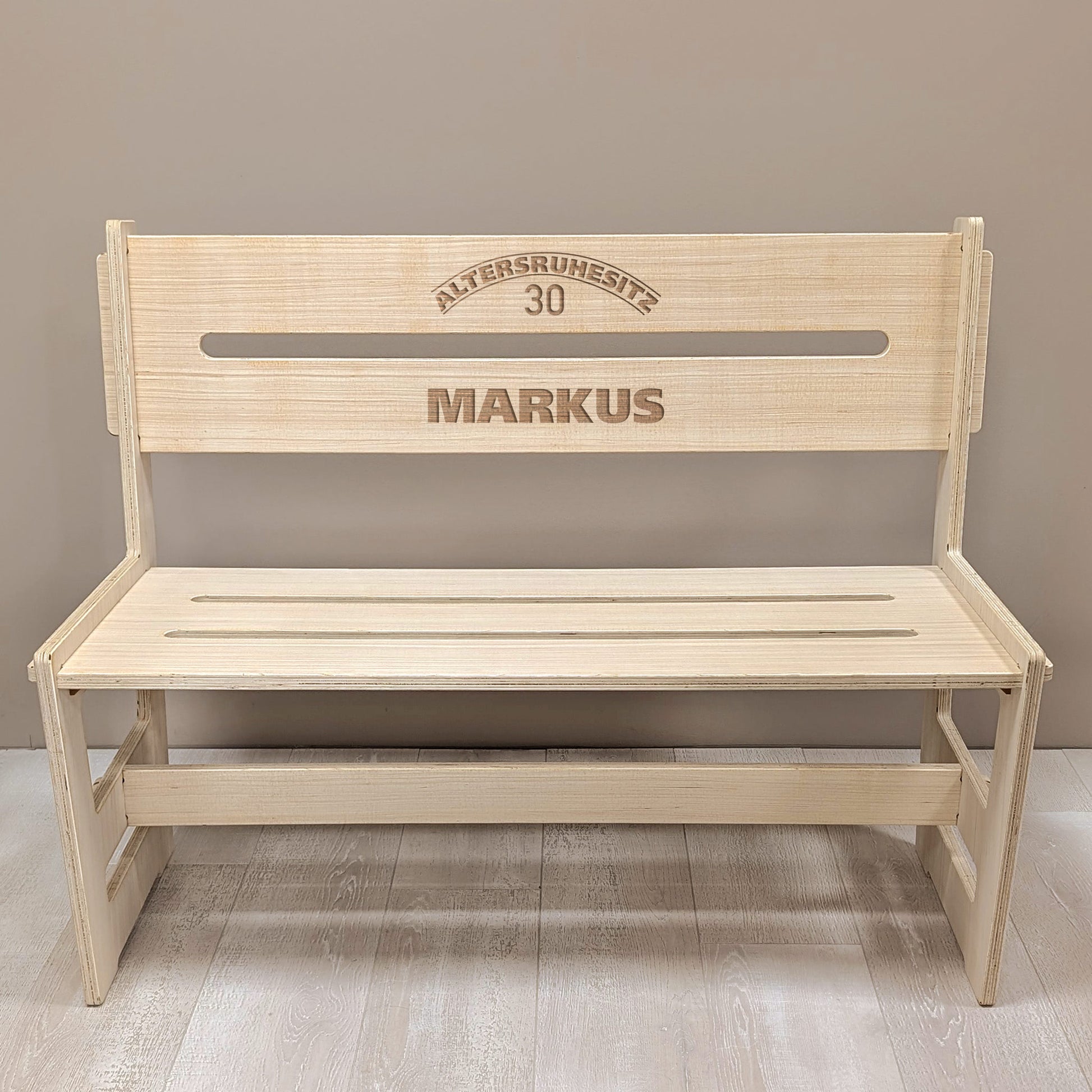 Ruhestandsbank aus Holz mit Gravur „Altersruhesitz 30 MARKUS“ – frontal aufgenommen auf hellem Boden