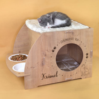 Katzenhaus in Eiche-Optik mit schlafender Katze auf dem oberen Kissen, Futterstation und personalisiertem Aufdruck