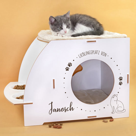 Weißes Katzenhaus mit personalisiertem Namen Janosch, rundem Eingang, Pfotenmotiv, Dachkissen und zwei Näpfen