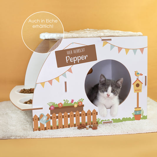 Weißes Katzenhaus mit Futterstation, Aufdruck Hier herrscht Pepper, Katzenbaby in der runden Öffnung und Hinweis auf Eiche-Variante