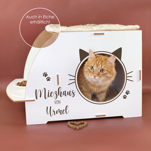 Weißes Katzenhaus mit personalisiertem Namen Urmel, Katze in runder Öffnung, Futterstation und Hinweis auf Eiche-Variante
